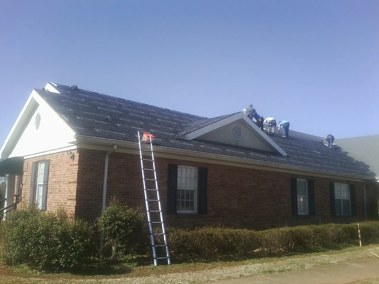 Crew tearing shingles off a brick ranch roof with a ladder set — Emergency Roof Repair work by our crew in Woodburn